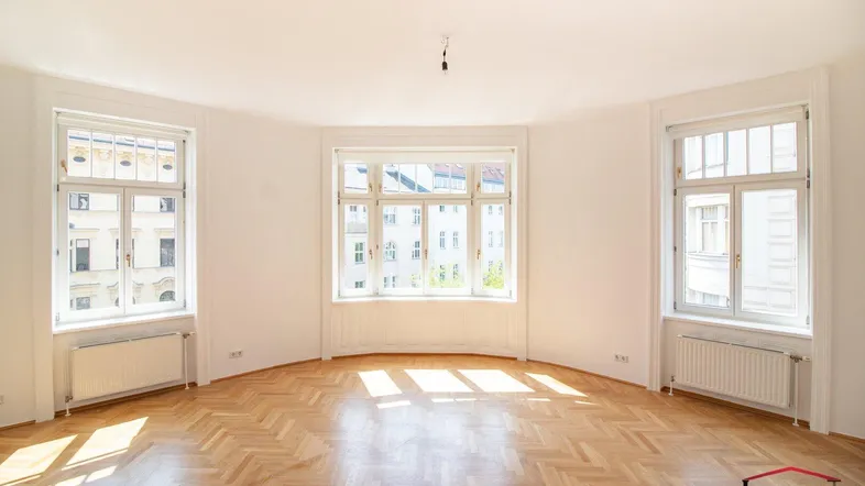 Heller Wohnraum mit Fischgrätparkett und großen Fenstern, die viel Tageslicht hereinlassen.