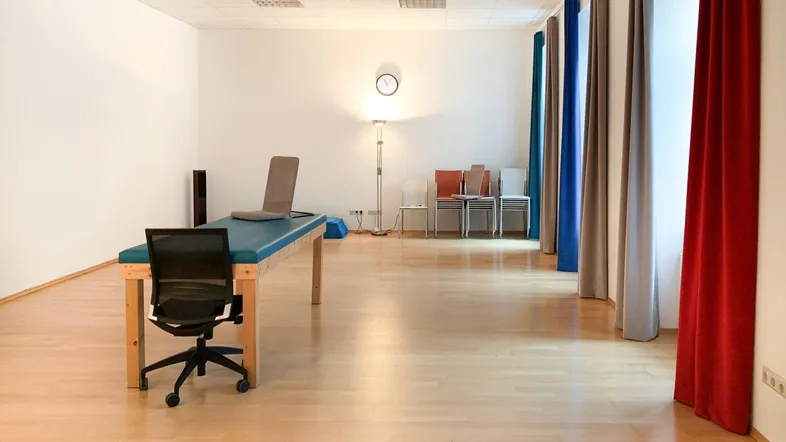 Geräumiger Büroraum oder Therapieraum mit hellem Holzfußboden und einfacher Einrichtung.