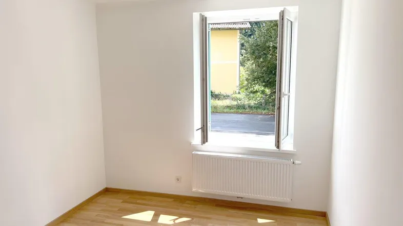Helles Zimmer mit Holzfußboden und Fensterblick ins Grüne, bereit zur individuellen Gestaltung.