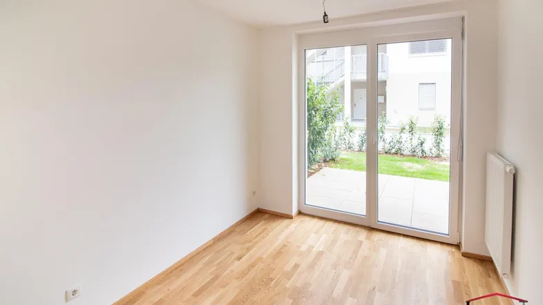 Helles Zimmer mit Parkettboden und Zugang zu einer kleinen Terrasse oder Gartenbereich.