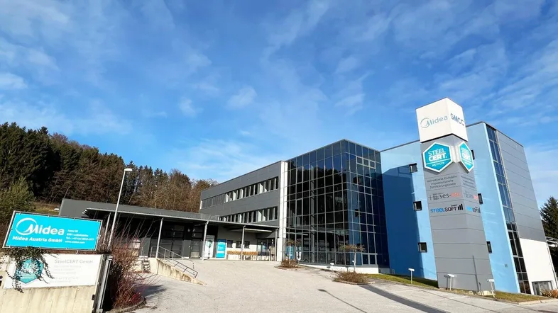 Modernes Bürogebäude mit Glasfassade und blauen Akzenten unter klarem Himmel.