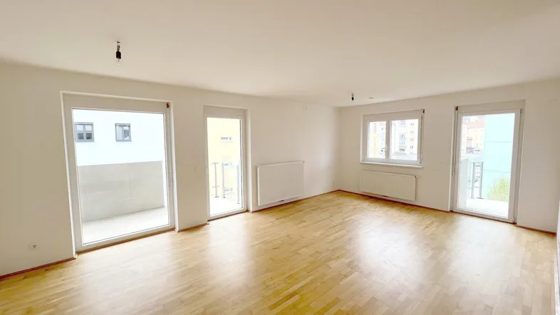 Helles, leeres Wohnzimmer mit Parkettboden und mehreren Zugängen zu Balkonen oder französischen Balkonen.