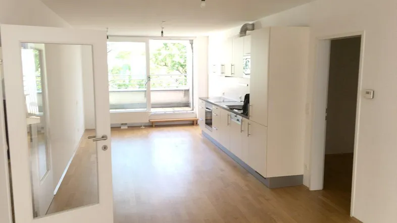 Heller offener Wohn- und Essbereich mit integrierter Küche, Parkettboden und Zugang zum Balkon.
