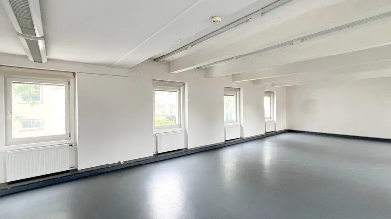 Geräumiger, leerer Büroraum mit mehreren Fenstern und grauem Bodenbelag, ideal für gewerbliche Nutzung.