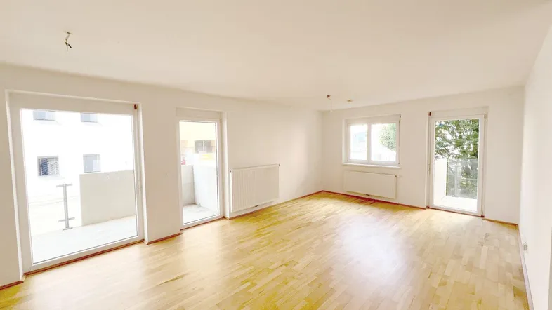 Helles, leeres Wohnzimmer mit Parkettboden und Zugang zu zwei Balkonen, ideal für individuelle Gestaltung.