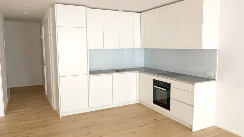 Moderne, helle Einbauküche mit weißen Fronten, integriertem Backofen und hellem Holzfußboden.