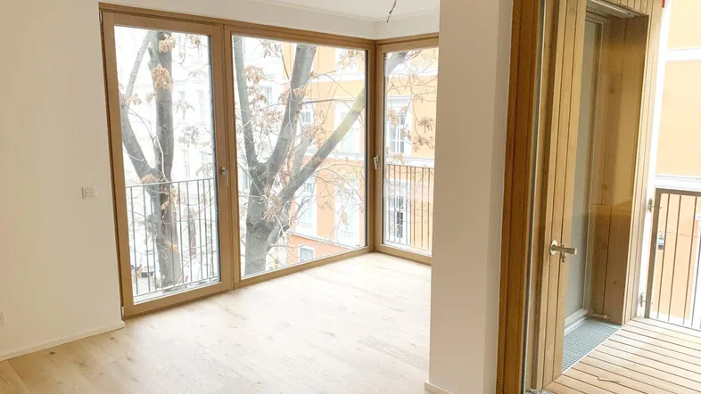 Helles Wohnzimmer mit Holzboden und großen Fenstern, die Zugang zu einem französischen Balkon bieten.