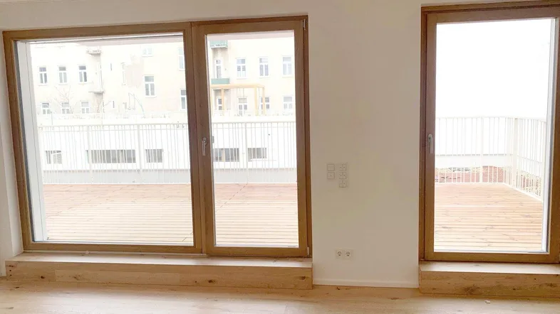 Helles Zimmer mit Holzboden und großen Fenstern, die Zugang zu einer Terrasse bieten.