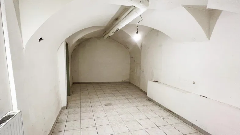 Geräumiger Kellerraum mit Gewölbedecke, Fliesenboden und sichtbaren Rohren an der Decke.