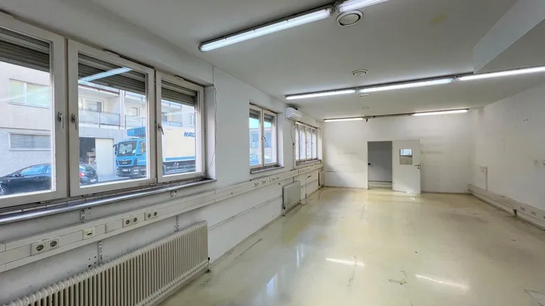Großer, heller Büroraum mit mehreren Fenstern, Heizkörpern und zahlreichen Steckdosen entlang der Wände.