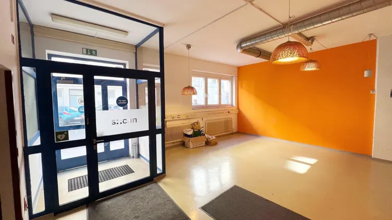 Heller Eingangsbereich eines Gewerbeobjekts mit großen Glastüren und orangefarbener Akzentwand.