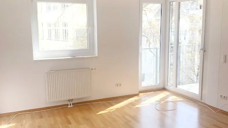 Helles Zimmer mit Parkettboden und Zugang zu einem Balkon, ideal als Wohn- oder Schlafbereich.