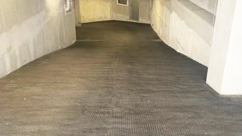 Einfahrtsrampe zu einer Tiefgarage mit Betonwänden und funktionaler Beleuchtung an der Decke.