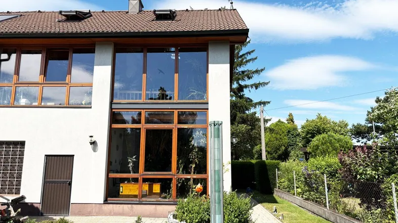 Moderne Hausfassade mit großen Glasflächen und Wintergarten unter blauem Himmel.