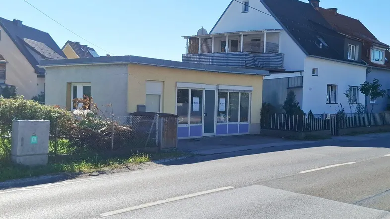 Ansicht des Gebäudes von der Straße mit einem kleinen Anbau und einem Balkon im Obergeschoss.