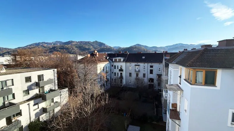 Panoramablick über die Stadt mit Bergen im Hintergrund unter klarem blauem Himmel.
