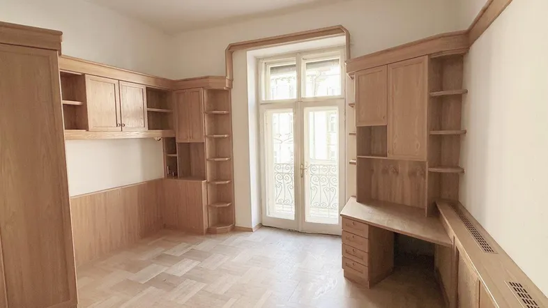 Helles Arbeitszimmer mit maßgefertigten Holzmöbeln, Parkettboden und Zugang zu einem französischen Balkon.