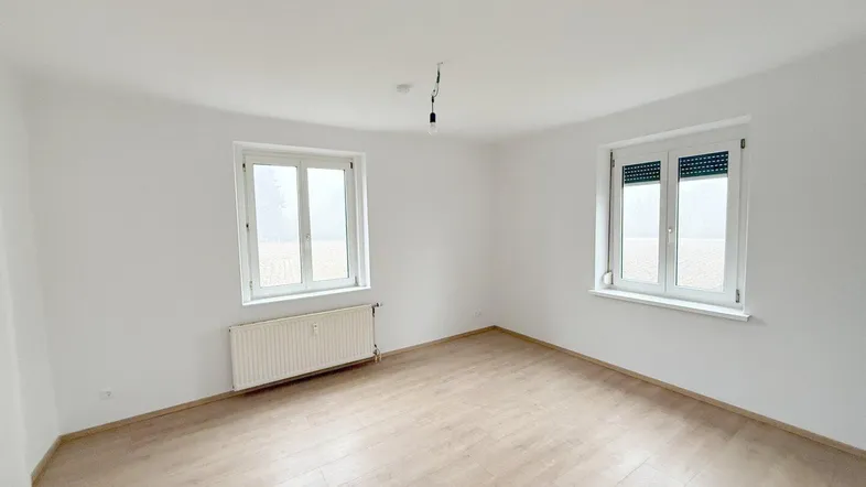 Helles Zimmer mit Laminatboden und zwei Fenstern, bereit zur individuellen Gestaltung.