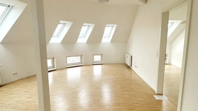 Heller, geräumiger Dachgeschossraum mit schrägen Wänden, vielen Dachfenstern und Parkettboden.