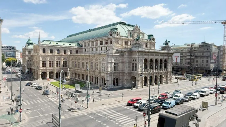 Großes, historisches Gebäude mit aufwendiger Architektur an einer belebten Stadtkreuzung unter blauem Himmel.