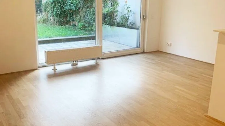 Helles Wohnzimmer mit Parkettboden und großzügigem Zugang zu einer Terrasse und dem Garten.