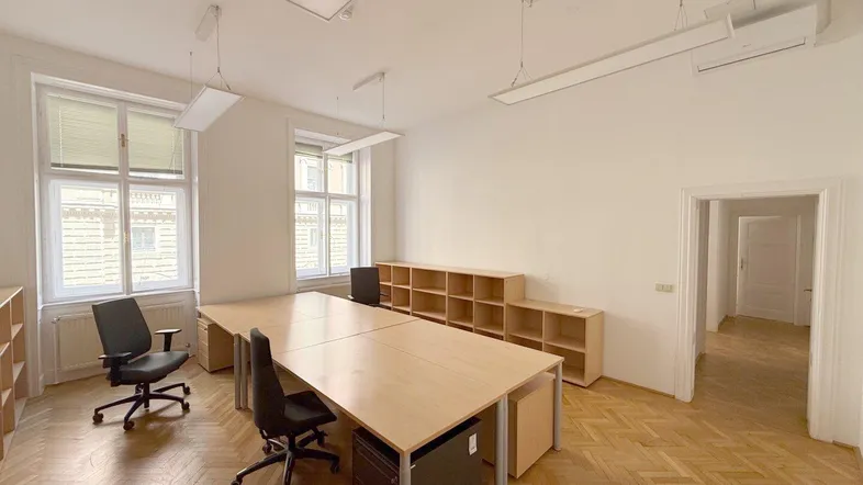 Geräumiges Büro mit mehreren Arbeitsplätzen, Holzparkett und großen Fenstern für viel Tageslicht.