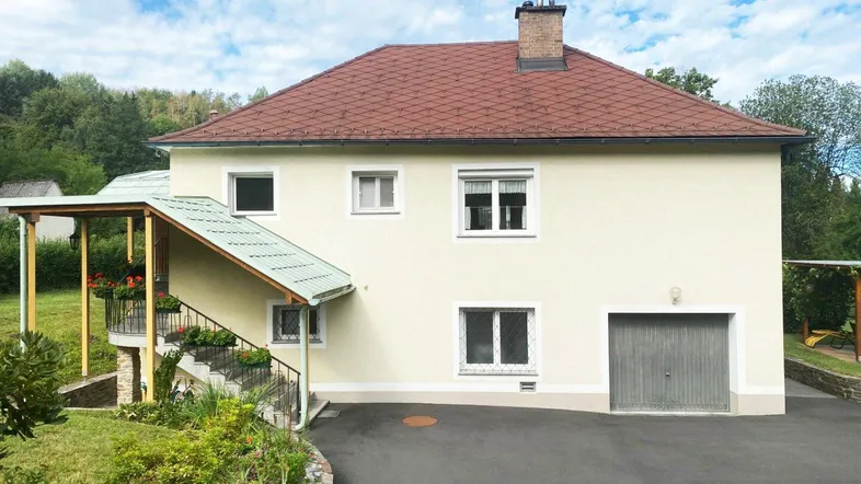 Ansicht des Hauses von der Seite mit Garagenzufahrt und gepflegtem Vorgarten unter blauem Himmel.