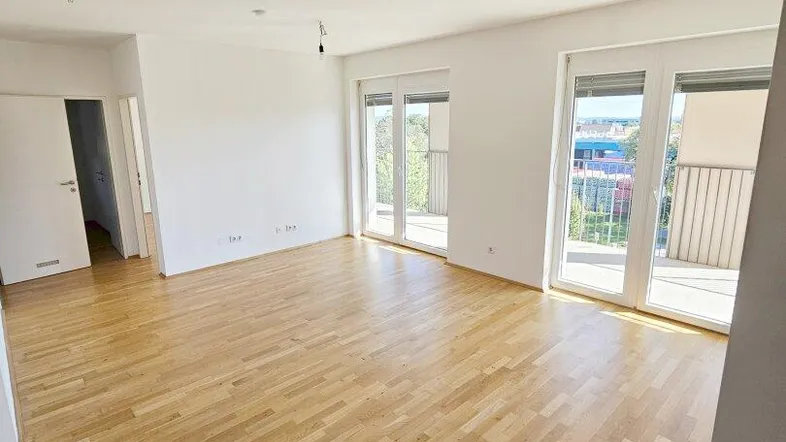 Helles Wohnzimmer mit Parkettboden und Zugang zu einem sonnigen Balkon, ideal für entspannte Stunden.