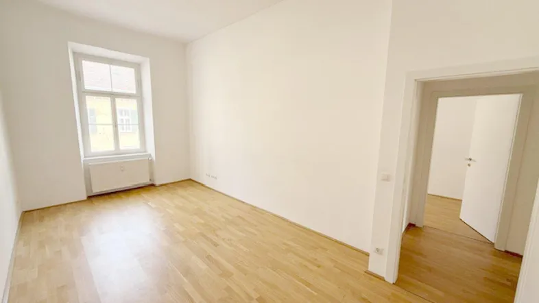 Helles, leeres Zimmer mit Parkettboden und weißen Wänden, bereit zur individuellen Gestaltung.