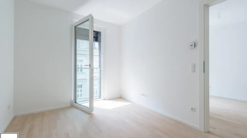Helles, leeres Zimmer mit Parkettboden und Zugang zu einem französischen Balkon.