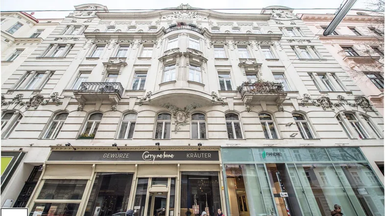 Ornate Fassade eines historischen Gebäudes mit Geschäften im Erdgeschoss und kleinen Balkonen.