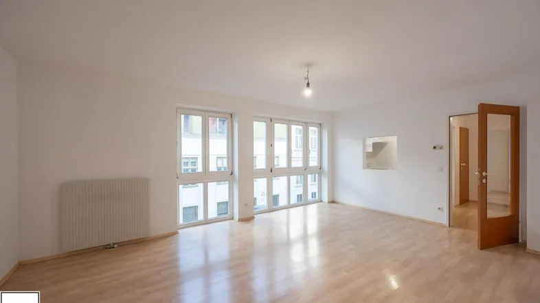 Helles Wohnzimmer mit großen Fenstern, Parkettboden und Heizkörper, bereit zur Einrichtung.