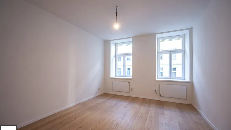 Helles, leeres Zimmer mit Parkettboden und zwei Fenstern, bereit zur individuellen Gestaltung.
