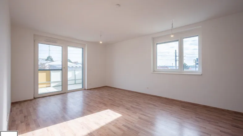 Helles, leeres Zimmer mit Laminatboden und Zugang zu einem Balkon, ideal als Wohnbereich.