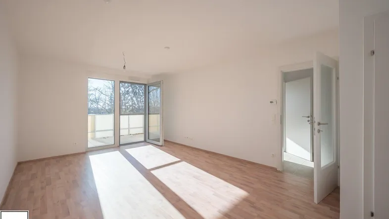 Helles Wohnzimmer mit Laminatboden und Zugang zu einem sonnigen Balkon.