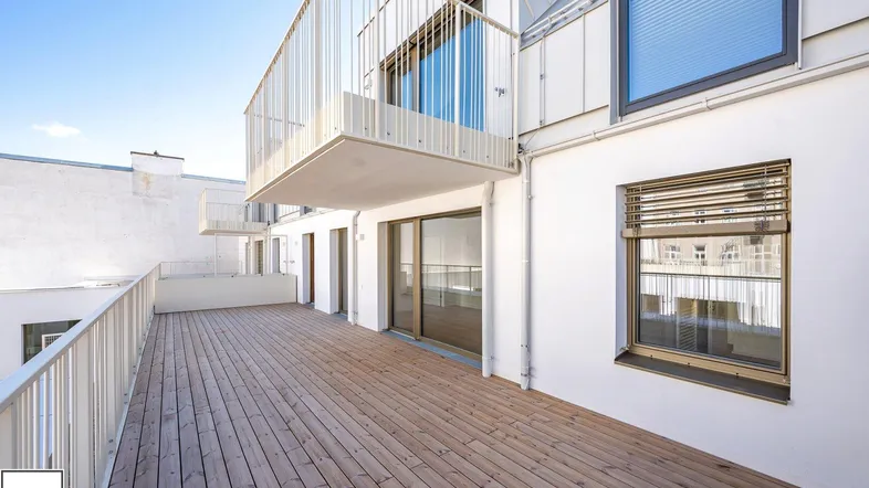 Große Holzterrasse mit Metallgeländer und Zugang zu den Wohnräumen eines modernen Gebäudes.