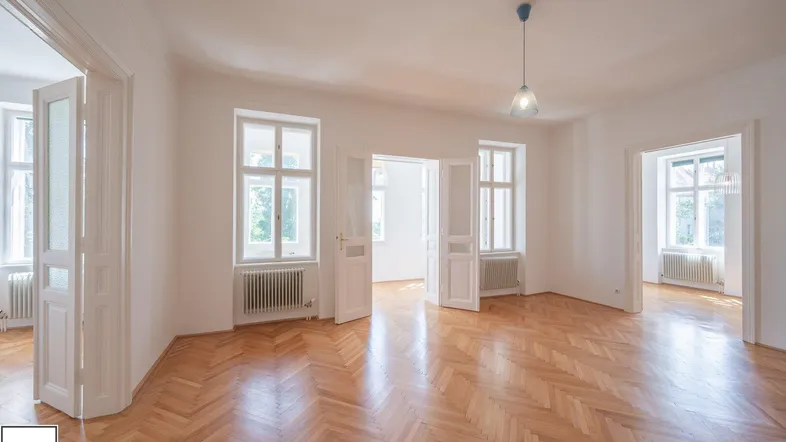 Helles Wohnzimmer mit Fischgrätparkett und hohen Fenstern, das mehrere Räume verbindet.