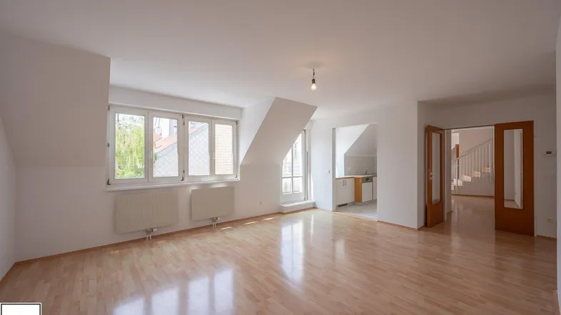 Helles Wohnzimmer mit Parkettboden, Dachschrägen und Zugang zu einer Küche sowie einem Treppenhaus.