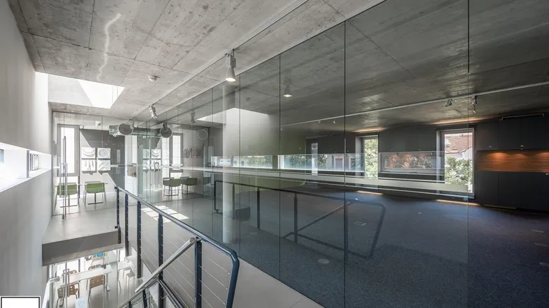Moderner Bürobereich mit unverputzten Betondecken, Teppichboden und Glaswänden, der viel natürliches Licht erhält.