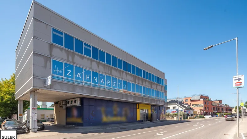 Modernes Geschäftsgebäude mit großen Fenstern und einer Zahnarztpraxis im oberen Stockwerk, direkt an einer Straße gelegen.