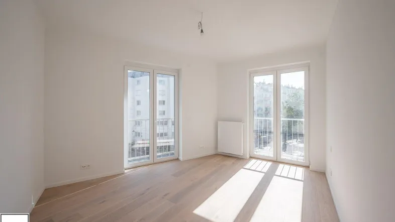 Helles Zimmer mit Holzboden und Zugang zu einem Balkon, durchflutet von natürlichem Sonnenlicht.
