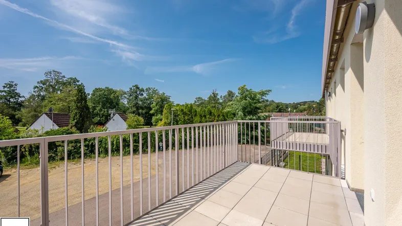 Geräumiger Balkon mit Fliesenboden und Blick ins Grüne unter blauem Himmel.