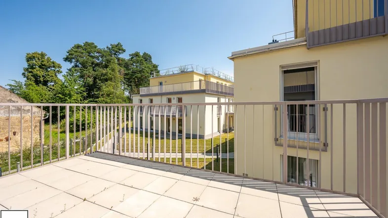 Geräumiger Balkon mit Fliesenboden und Blick auf die umliegenden Neubauten und Grünflächen.