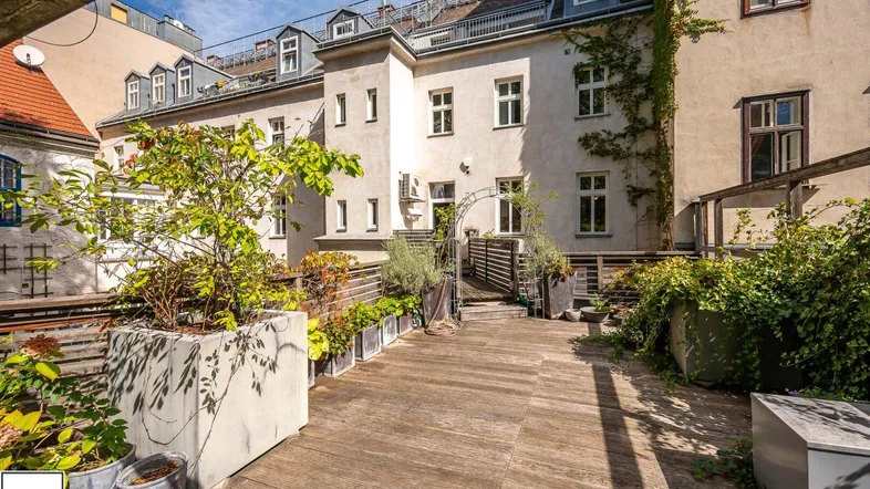 Weitläufige Holzterrasse mit Pflanzenkübeln und Blick auf die historische Gebäudefassade.