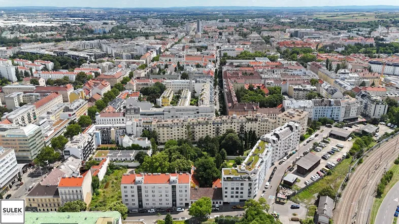 Weitläufige Luftaufnahme einer städtischen Wohngegend mit vielen Gebäuden und ausgedehnten Grünflächen.