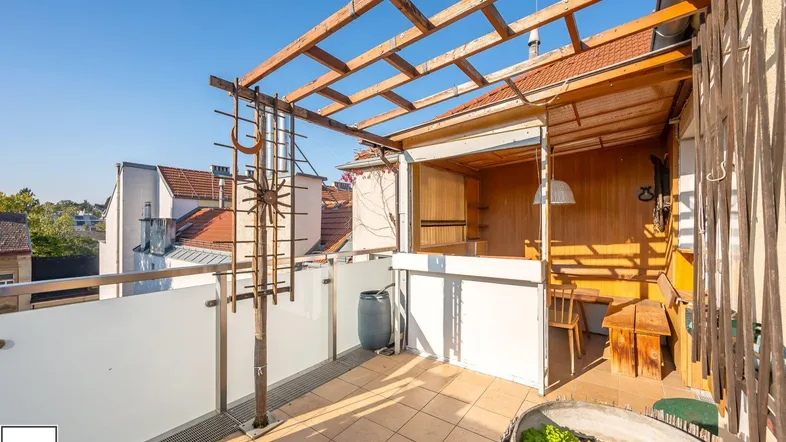 Sonnige Dachterrasse mit Holzpergola, Fliesenboden und weitem Blick über die Dächer der Stadt.