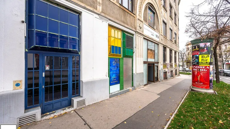 Erdgeschossfassade eines Altbaus mit bunten Schaufenstern und einem Bürgersteig in der Stadt.