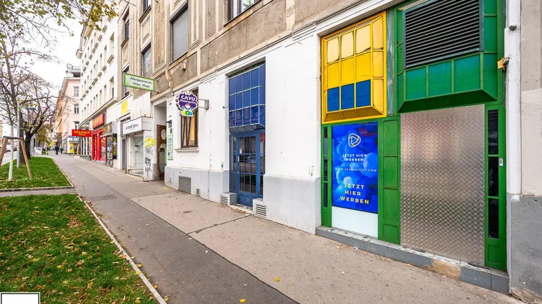 Ansicht der Geschäftsfassade mit bunten Schaufenstern und einem Gehweg in städtischer Umgebung.