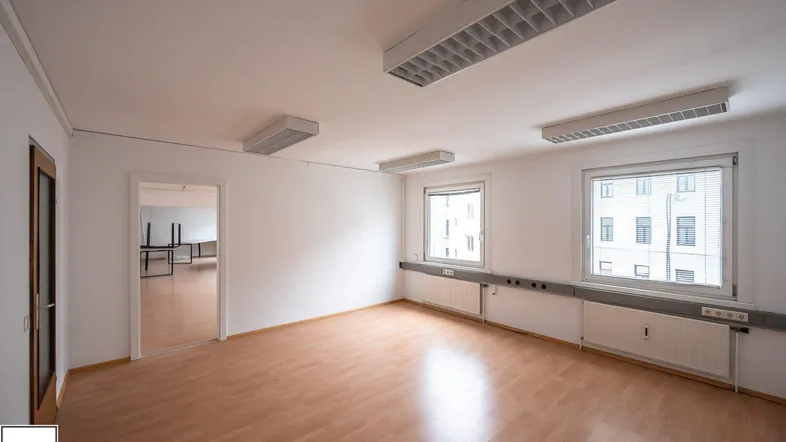 Heller Büroraum mit Holzfußboden und großen Fenstern, bereit zur individuellen Gestaltung.