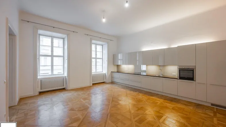 Moderne, offene Wohnküche mit glänzenden Schränken, Parkettboden und großen Fenstern.